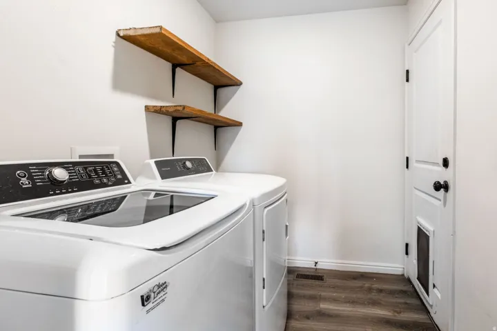 Laundry area featuring wood-finish flooring, white walls, and two rustic wood-plank shelves with black metal brackets