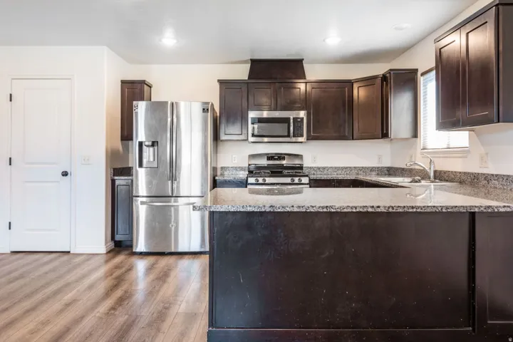 Kitchen featuring wood-finish flooring, dark wood cabinetry, stainless steel appliances, and granite countertops