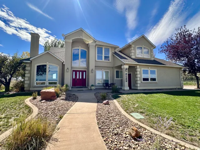 Stucco exterior with decorative trim, prominent red double entry doors, multiple large windows, and a structured walkway leading to the entrance