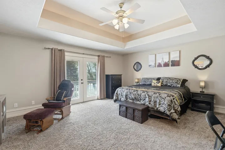 Tray ceiling with ceiling fan, double French doors, wall-to-wall carpeting, and neutral wall tones