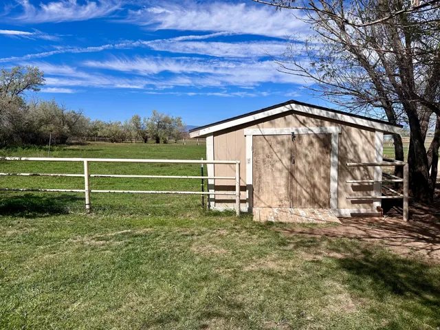 Storage shed with dual wood doors, a sloped roof, and a fenced enclosure