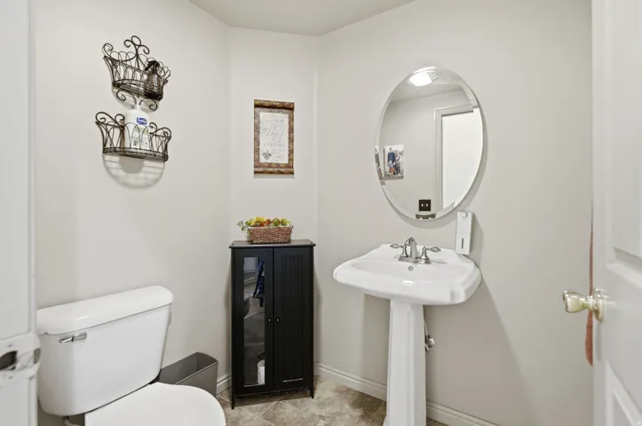 Pedestal sink with chrome fixtures, oval mirror, and a built-in toilet