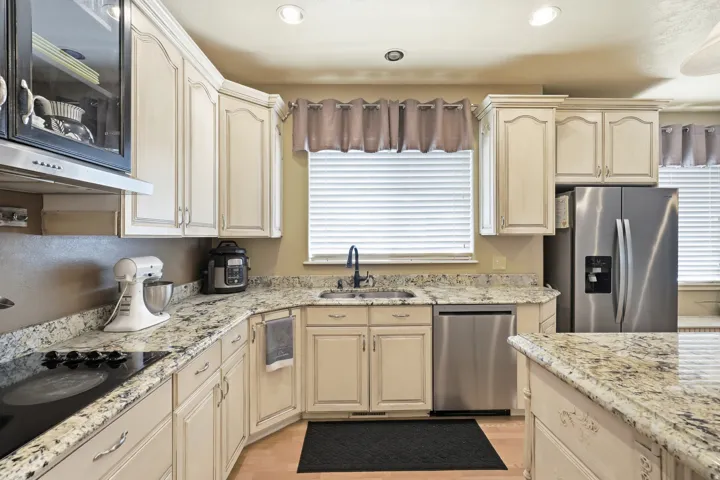 Kitchen featuring light-toned cabinetry, granite countertops, stainless steel appliances, and a built-in cooktop