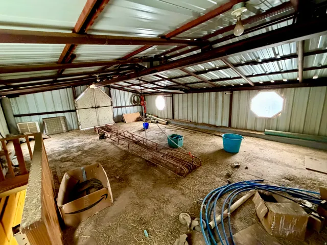 Large, open barn interior featuring a metal roof, exposed structural beams, corrugated metal walls, and multiple octagonal windows