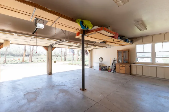 Concrete flooring garage with dual automatic garage doors, integrated overhead storage, built-in cabinetry, and multiple windows