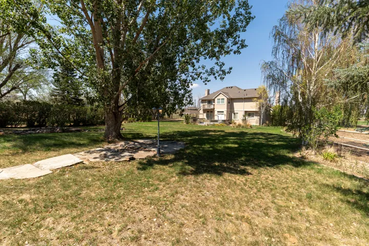 Expansive rear yard with mature trees, established shrubs, and a neutral-toned two-story residence featuring multiple windows and a balcony