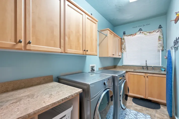 Laundry area with light wood-finish cabinetry, granite-style countertops, and a utility sink