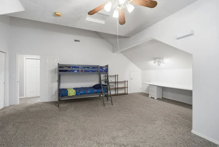 Vaulted ceiling, ceiling fan, skylight, built-in desk, and grey carpeting