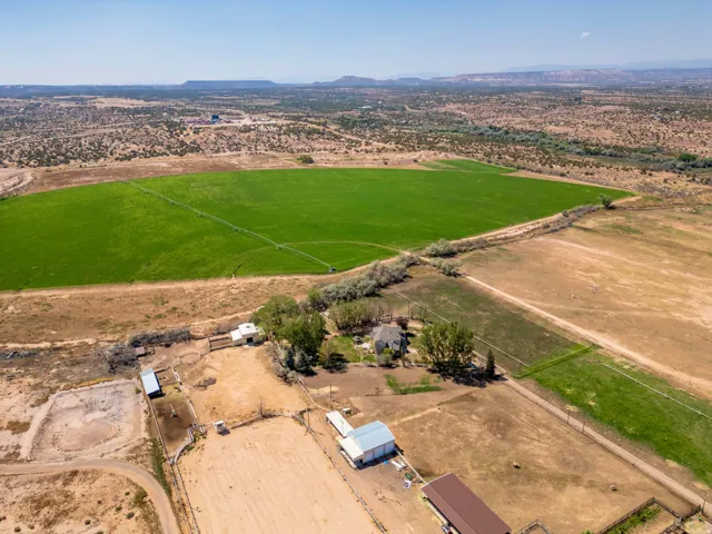 Expansive land featuring a large green field with irrigation, a residence, multiple outbuildings, and an equestrian arena
