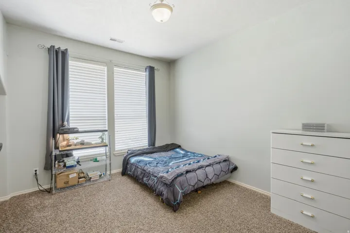 Neutral wall paint, textured ceiling, two large windows with blinds, and light brown carpet flooring