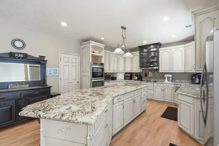Kitchen featuring a large island with stone countertops, recessed lighting, double wall ovens, and wood-finish flooring