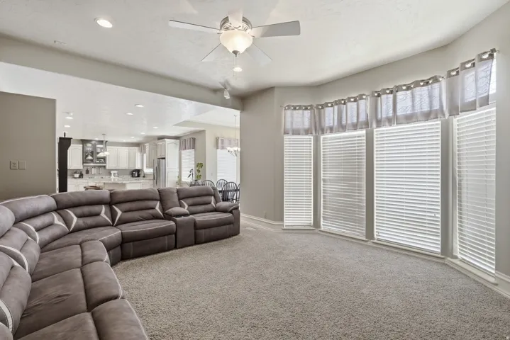 Spacious entertainment room featuring a curved sectional layout, neutral carpet flooring, and abundant natural light from multi-panel glass doors with motorized blinds