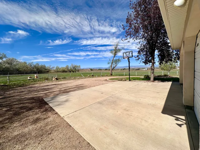 Spacious concrete pad, basketball hoop, mature trees, and expansive grassy area with fencing