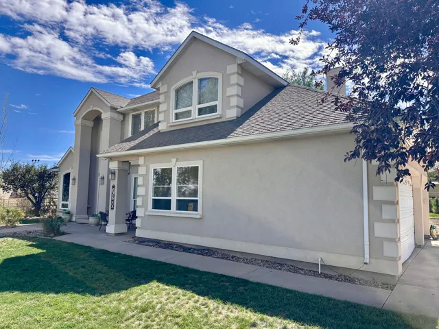 Stucco exterior with a pitched roof, prominent arched entryway, multiple window styles, and an attached garage with decorative paneling