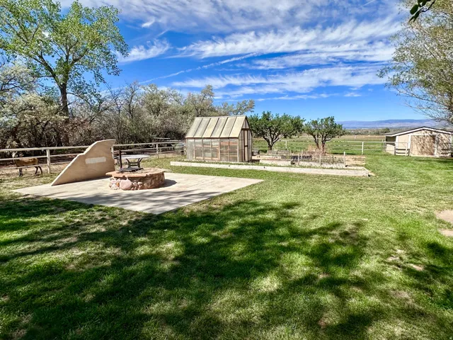 Expansive lawn area featuring a concrete patio with a stone fire pit, a greenhouse structure, and a utility shed