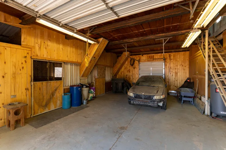 Barn interior featuring wood plank walls, concrete flooring, exposed wood beams, and fluorescent lighting