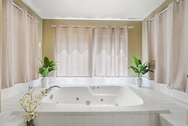 Integrated soaking tub with chrome fixtures, surrounded by white tile and light-toned wall paint