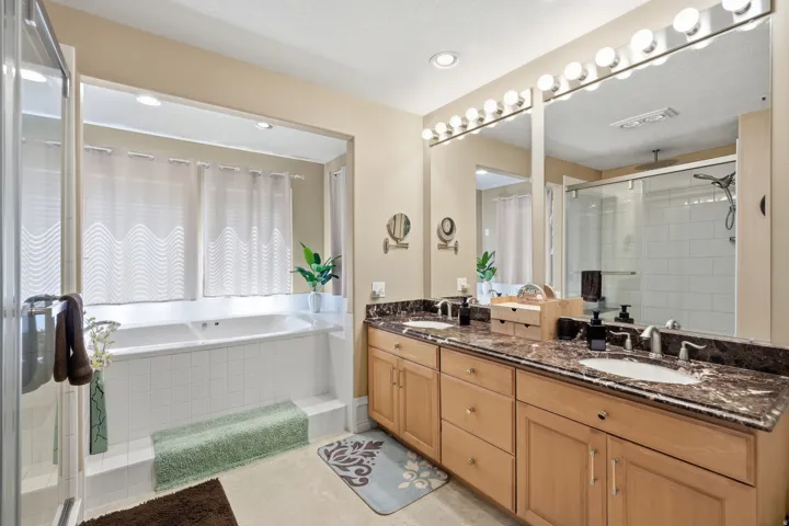 Dual vanity with stone countertop, large soaking tub, separate glass-enclosed shower, and built-in cabinetry