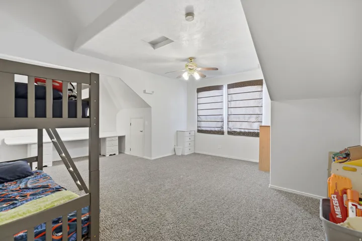 Spacious room featuring vaulted ceilings, textured carpeting, a ceiling fan with integrated lighting, and multiple windows with blinds