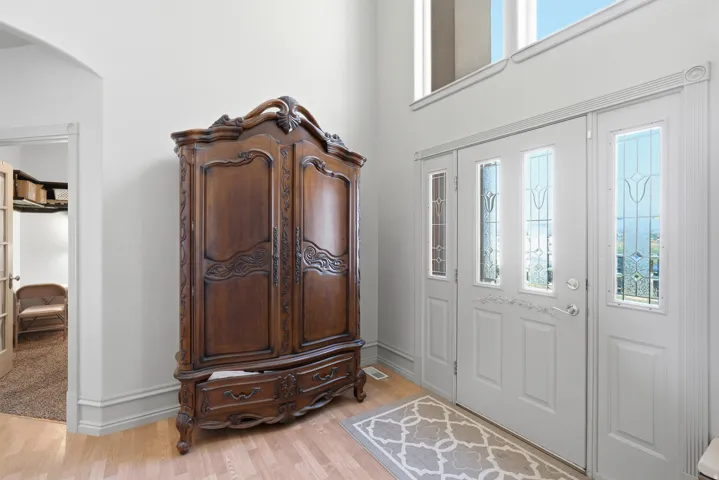 Double entry doors with decorative glass panels, transom windows, light wood-finish flooring, and crown molding