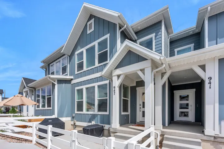Contemporary townhome facade with blue vertical siding, white trim, prominent gables, covered entryways, and multi-pane windows