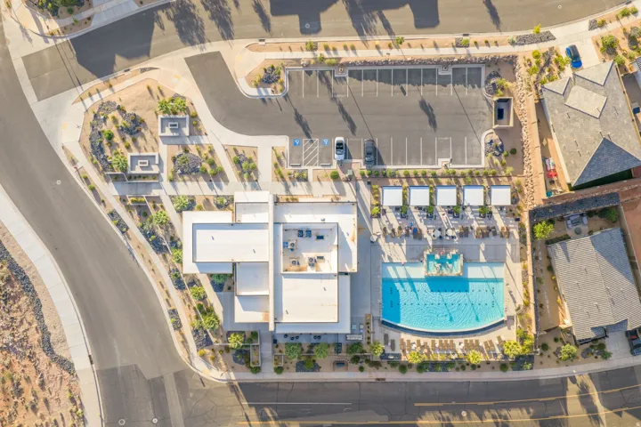 Outdoor swimming pool with built-in fountains, surrounding lounge seating with individual awnings, dedicated parking lot, and adjacent paved roadways