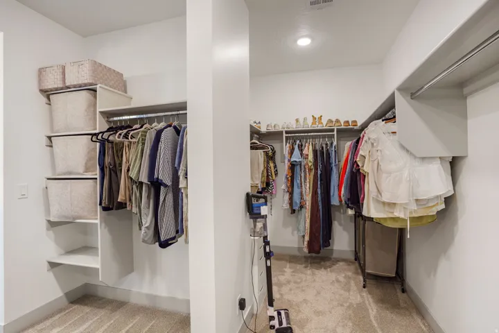 Spacious walk-in closet featuring extensive built-in shelving, multiple hanging rods, recessed lighting, and soft carpet flooring