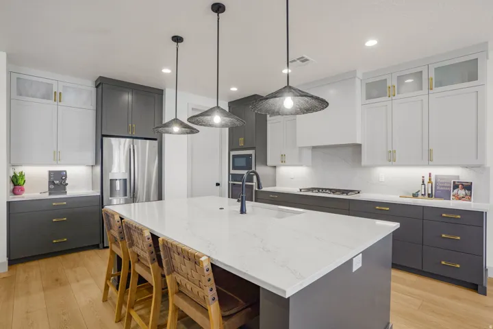 Spacious kitchen featuring a large central island with a sink, stainless steel appliances, two-tone cabinetry, light-toned countertops with a matching backsplash, and wood-finish flooring