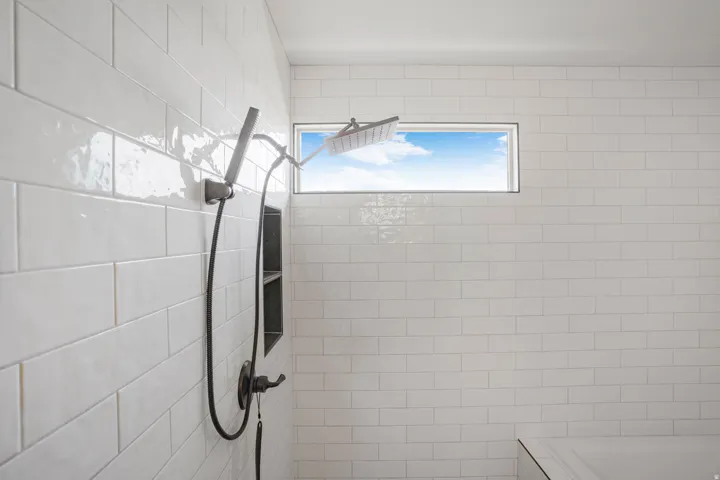 Shower enclosure with white subway tile, a fixed rainfall showerhead, and a handheld spray attachment