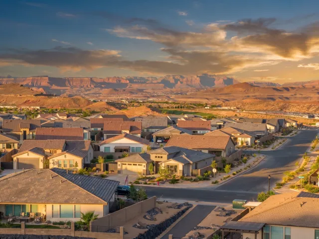 Residential neighborhood featuring varied single-story homes with tile roofs, concrete driveways, and xeriscaped landscaping, set against a distant mountain range