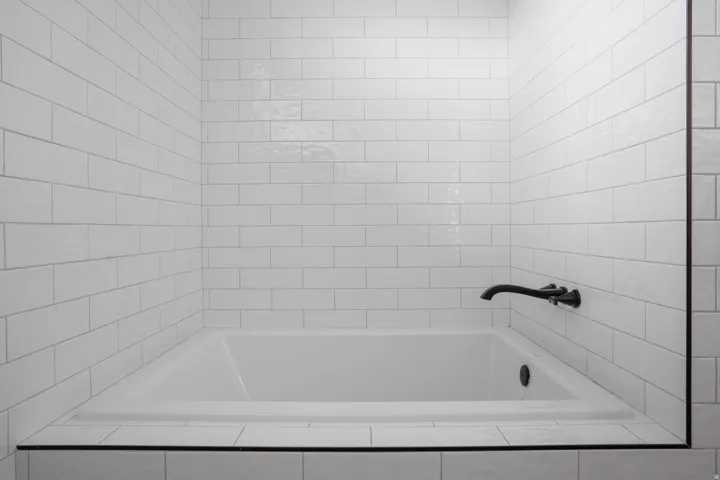 Built-in soaking tub with white subway tile surround and a matte black wall-mounted faucet