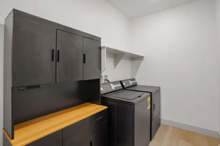 Laundry area featuring black cabinetry with a light wood-finish countertop, white walls, and wood-finish flooring