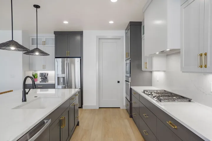 Modern kitchen featuring a large island with an undermount sink, two-tone cabinetry, quartz countertops, and stainless steel appliances including a gas cooktop and double ovens