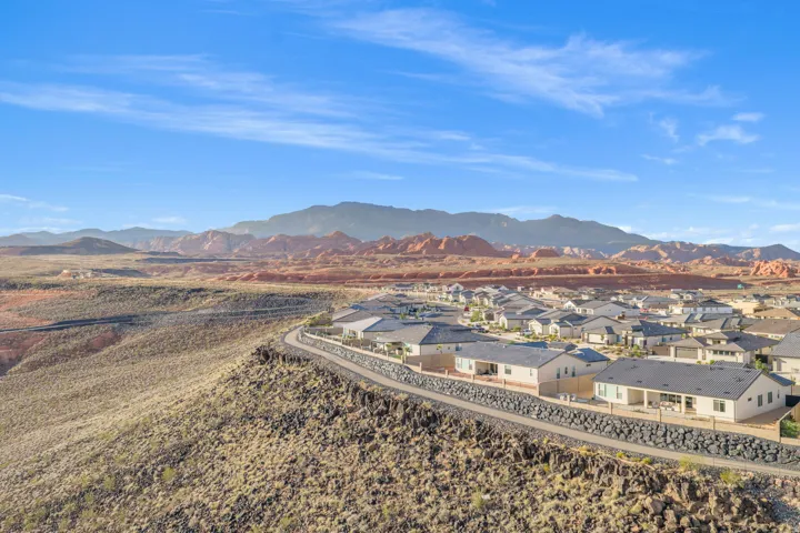 Expansive desert landscape featuring a residential community with contemporary homes, varied rooflines, and a paved road bordering the development