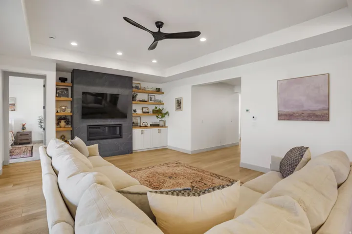 Living area featuring a floor-to-ceiling dark stone fireplace with a built-in firebox, light wood-finish flooring, and white walls