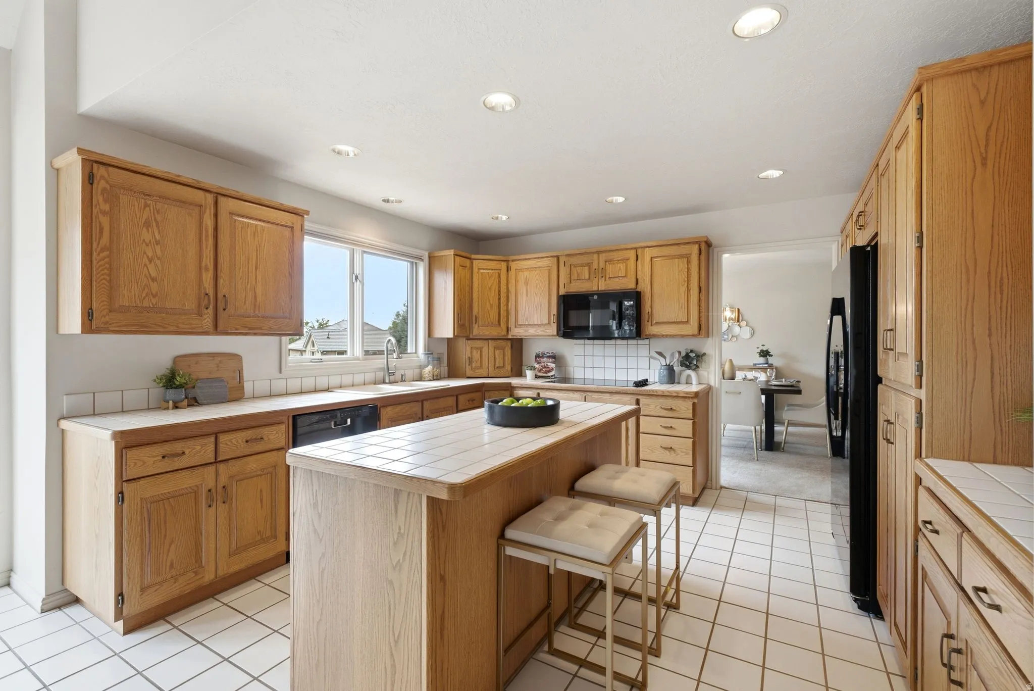 Kitchen featuring extensive wood cabinetry, a tiled island with breakfast bar seating, recessed lighting, and a window above the sink