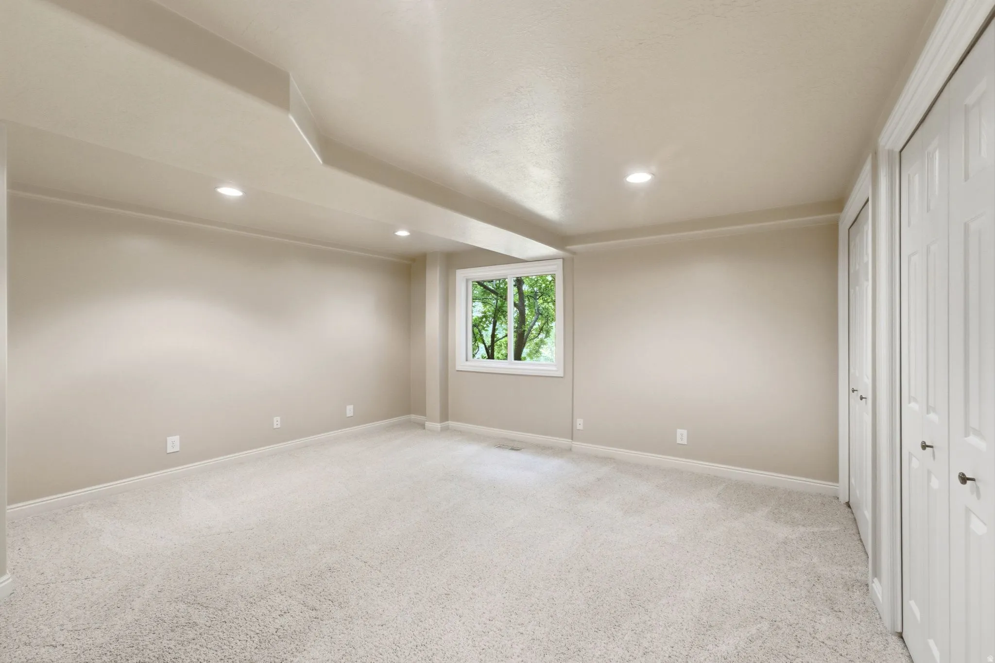 Carpeted room featuring a single window, recessed lighting, and two bi-fold closet doors