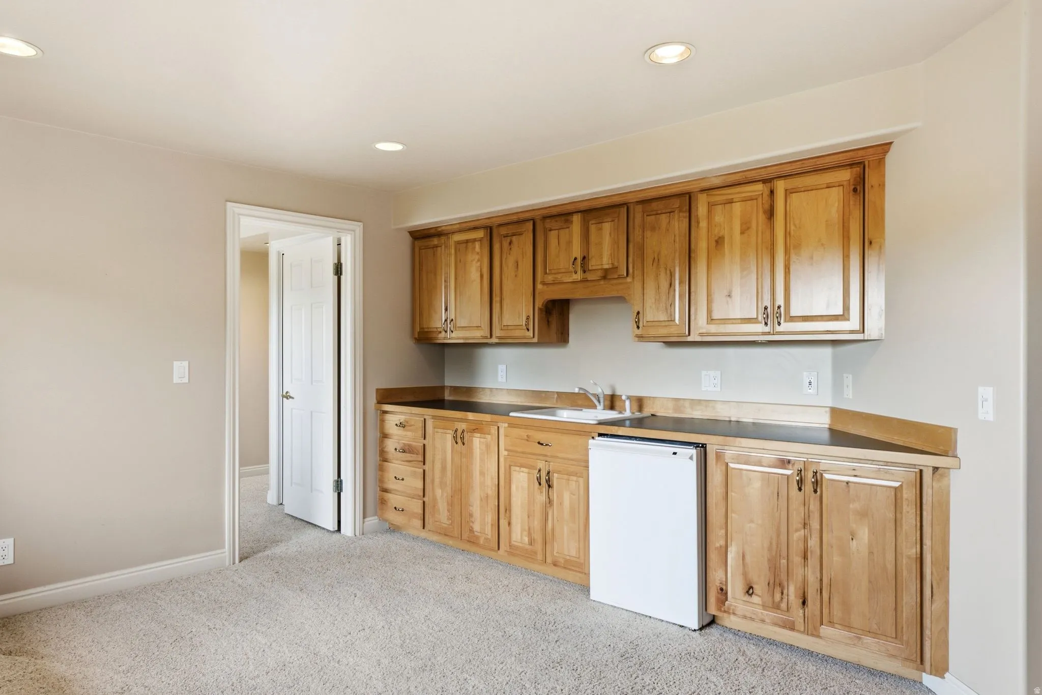 Built-in kitchenette featuring light wood cabinetry, dark countertops, an undermount sink, and a compact refrigerator