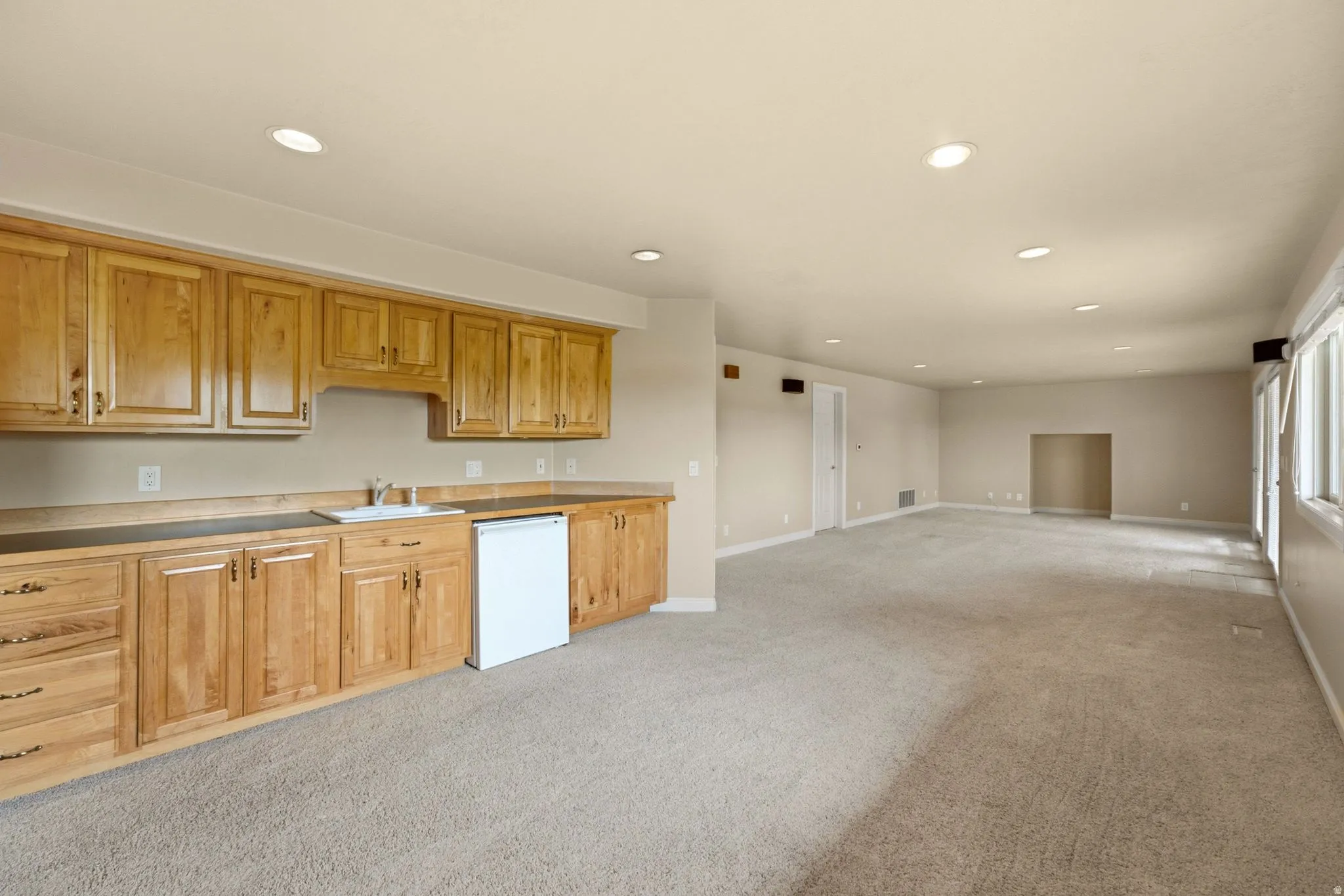 Integrated wet bar featuring a sink, wood cabinetry, and a compact refrigerator