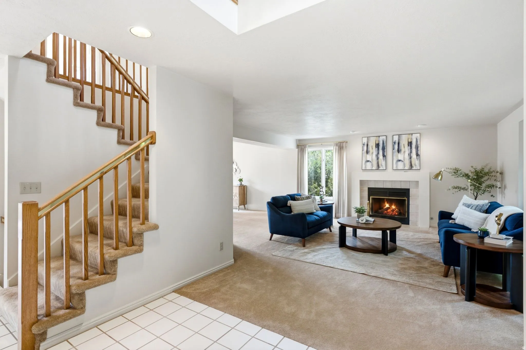Inviting living area featuring a fireplace with a white mantel, large window with sheer curtains, and light-toned carpeting