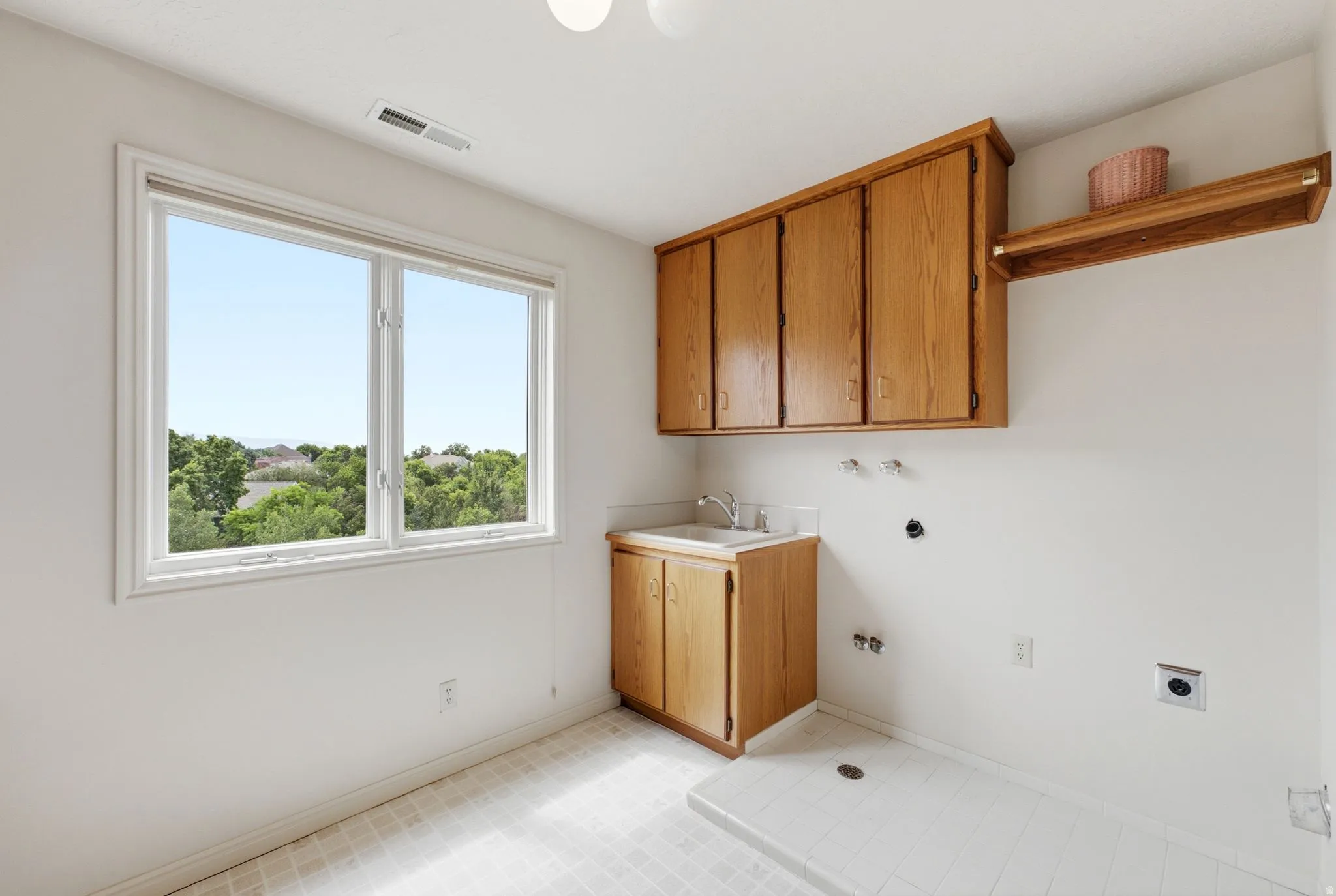Utility room featuring a double window, wood-finish cabinetry, a utility sink, and a tiled floor with a floor drain