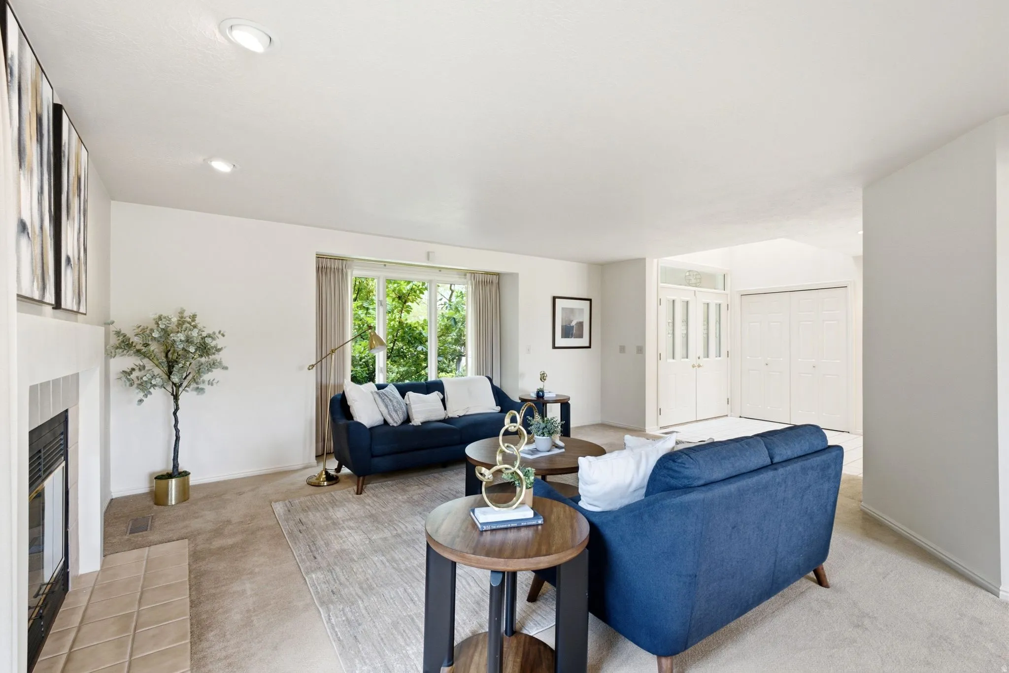 Carpeted living space featuring a fireplace with a tile hearth and surround, recessed lighting, and a large window overlooking exterior greenery