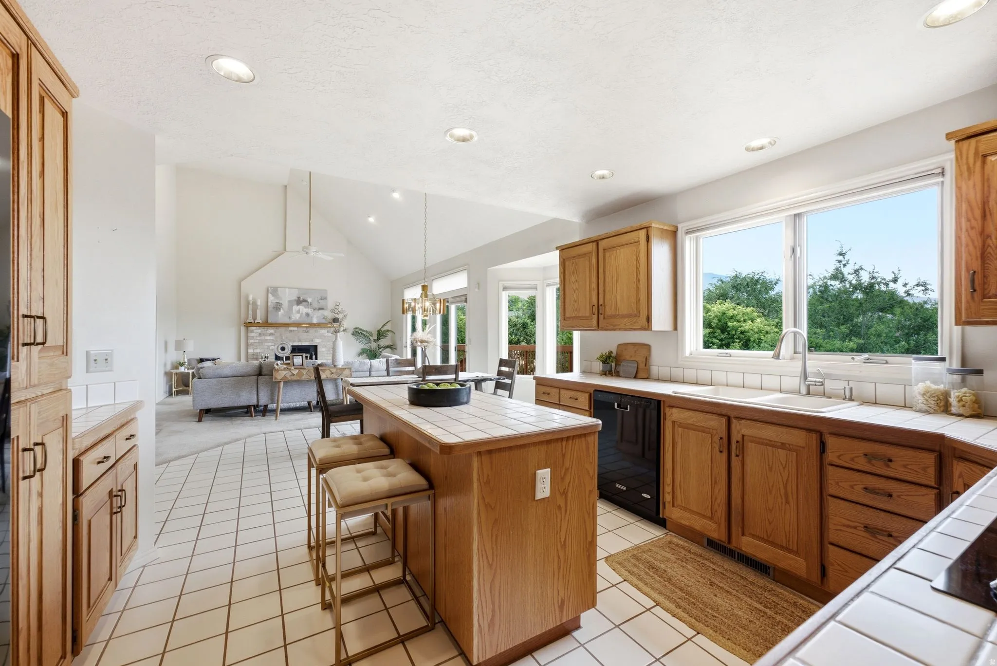 Bright kitchen featuring wood cabinetry, white tile countertops, a large window overlooking trees, a tile backsplash, and recessed lighting