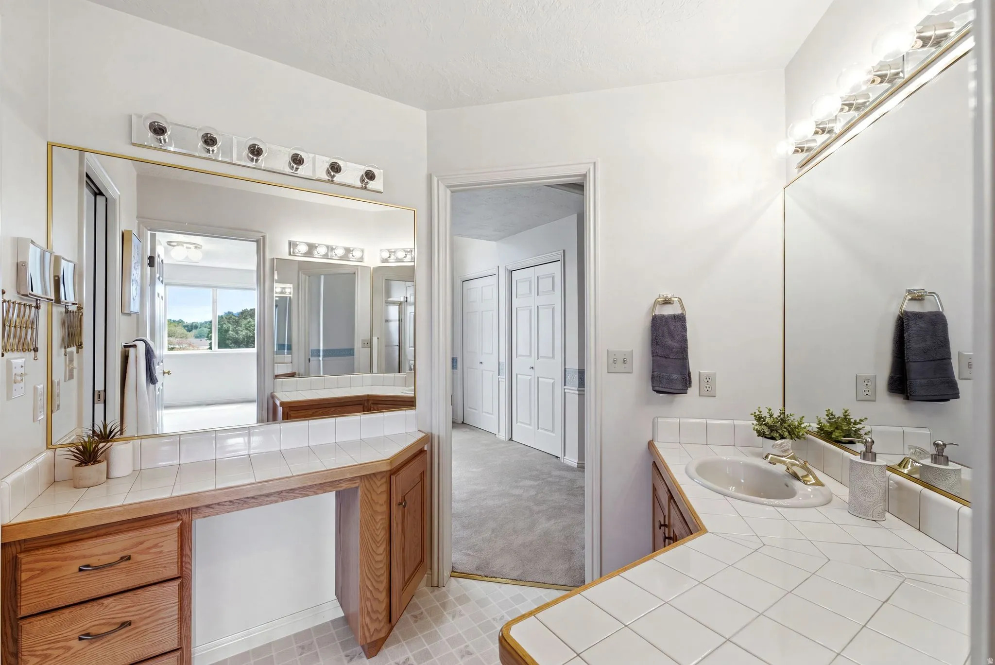 Bathroom vanity featuring light wood cabinetry, white tile countertops, and integrated sink