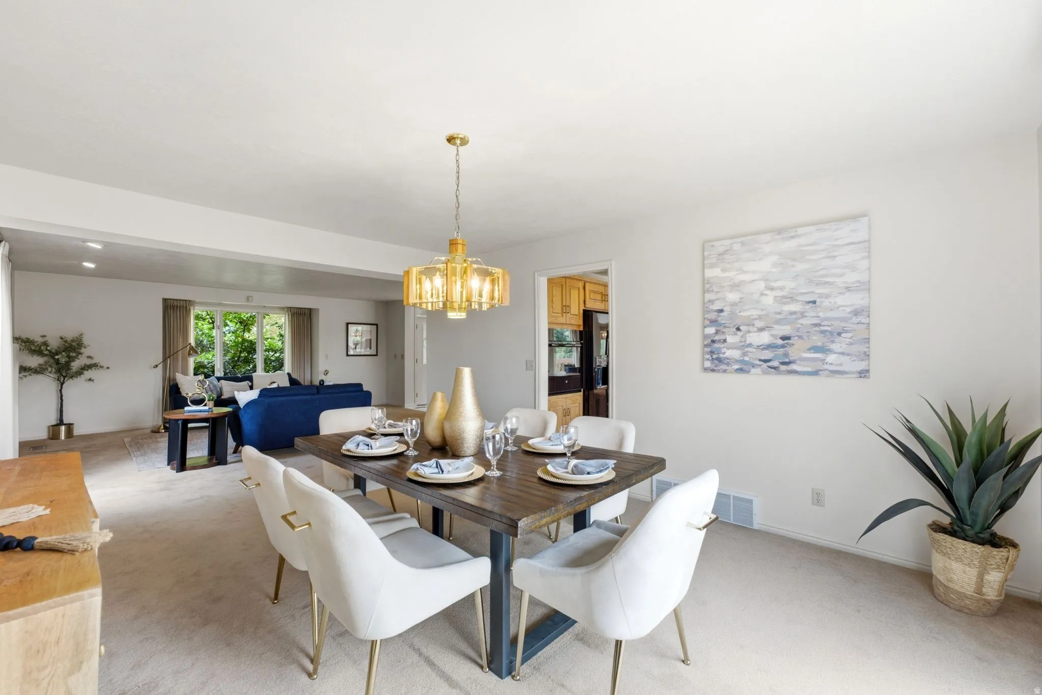 Open-concept living area featuring a dining space with a rectangular wood-finish table, a gold-tone chandelier, and light-colored walls