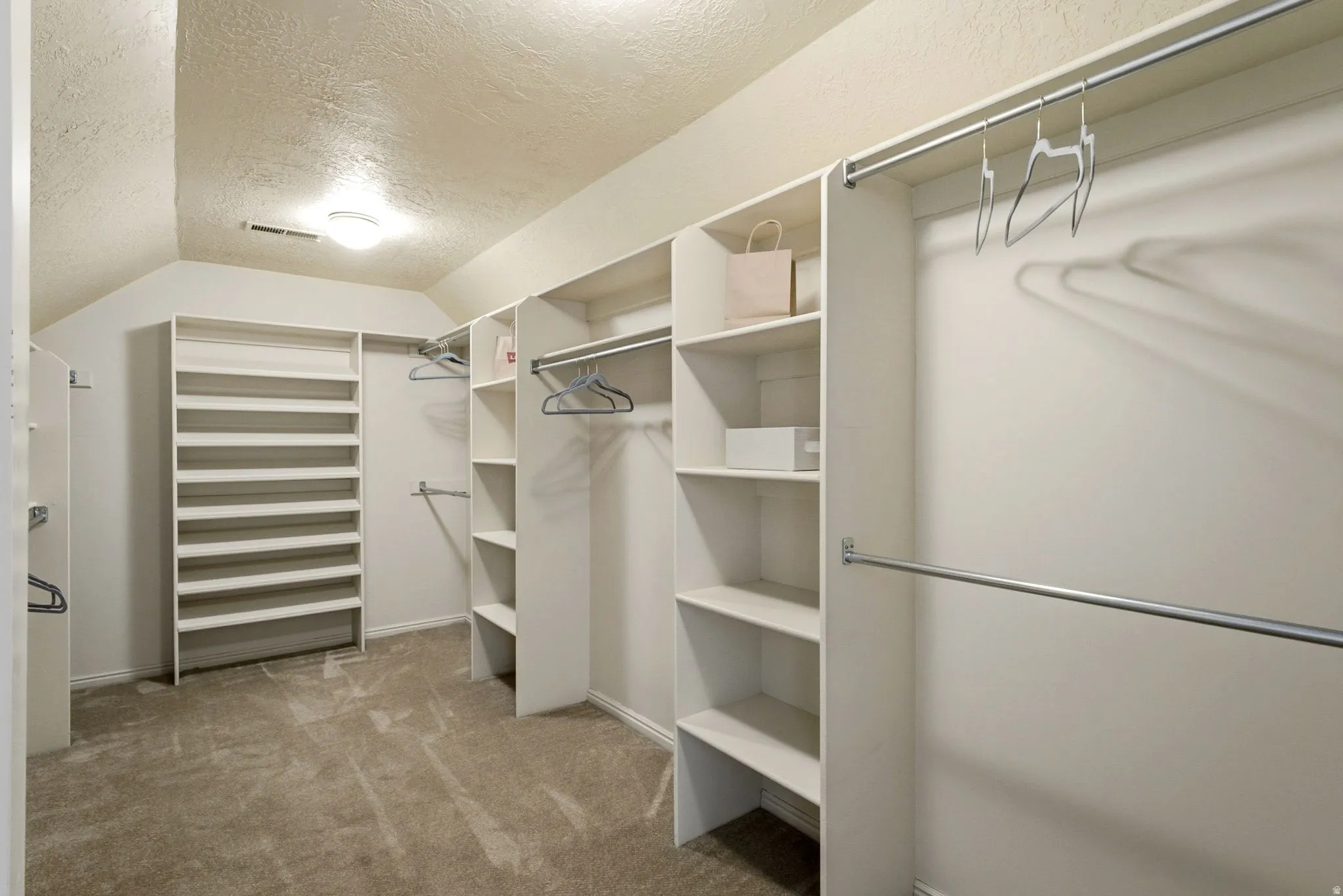 Expansive closet with built-in shelving, multiple hanging rods, and recessed lighting