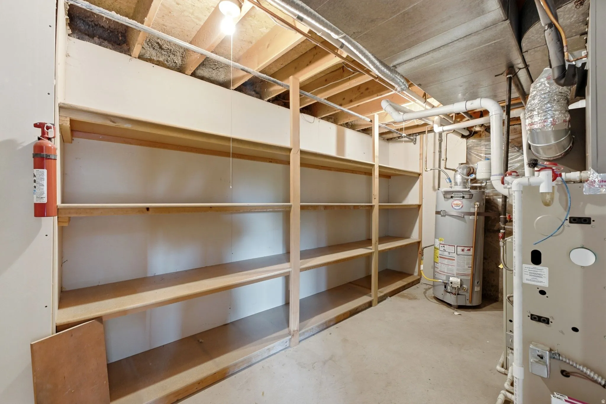 Utility room featuring extensive built-in wooden shelving, exposed ceiling joists, and concrete flooring