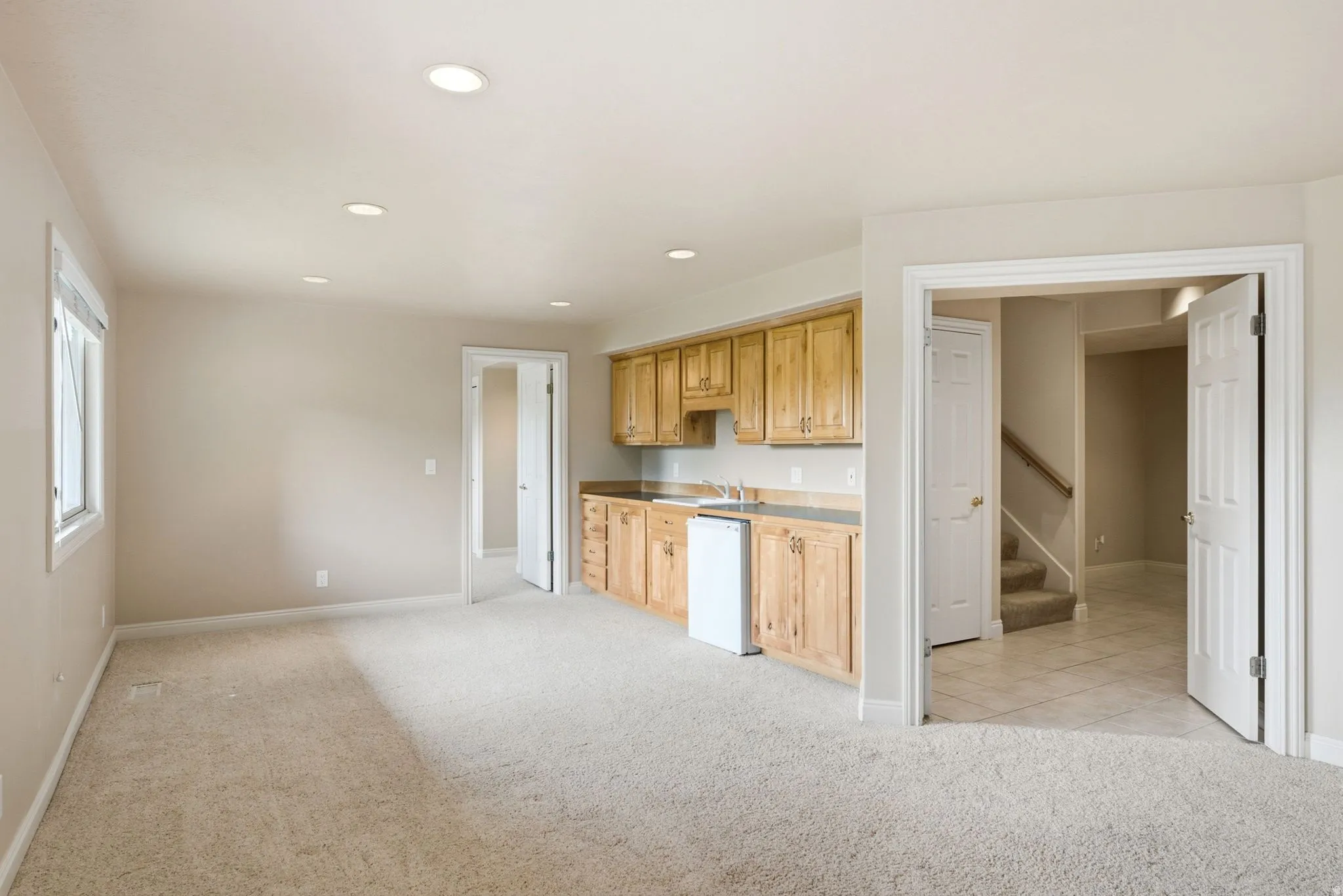 Spacious carpeted room featuring a built-in wet bar with wood cabinetry, a sink, and an under-counter appliance