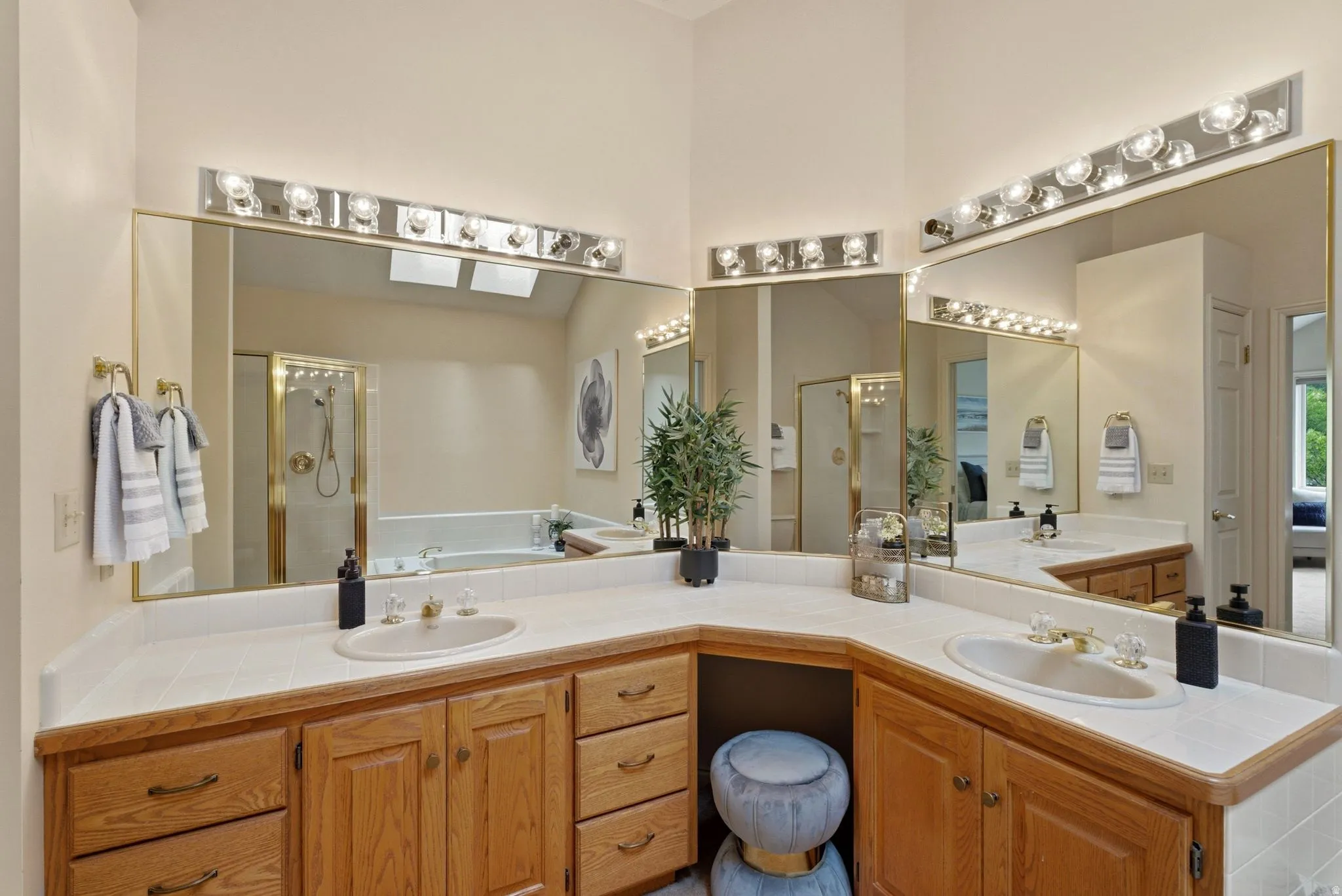 Dual vanity with integrated sinks, ample wood cabinetry, large mirrors with overhead lighting, and a built-in vanity area