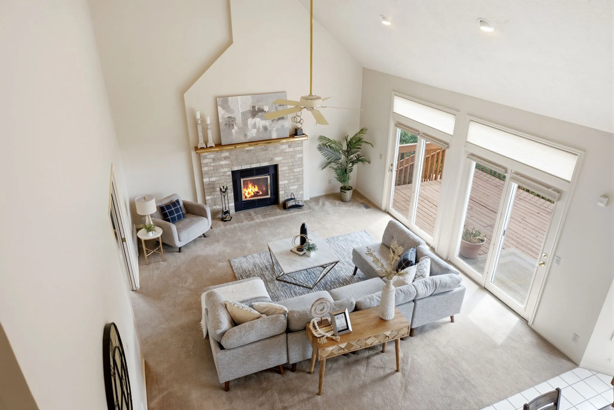 Vaulted ceiling living room featuring a brick fireplace with wood mantel, multiple glass sliding doors to outdoor decking, and recessed lighting